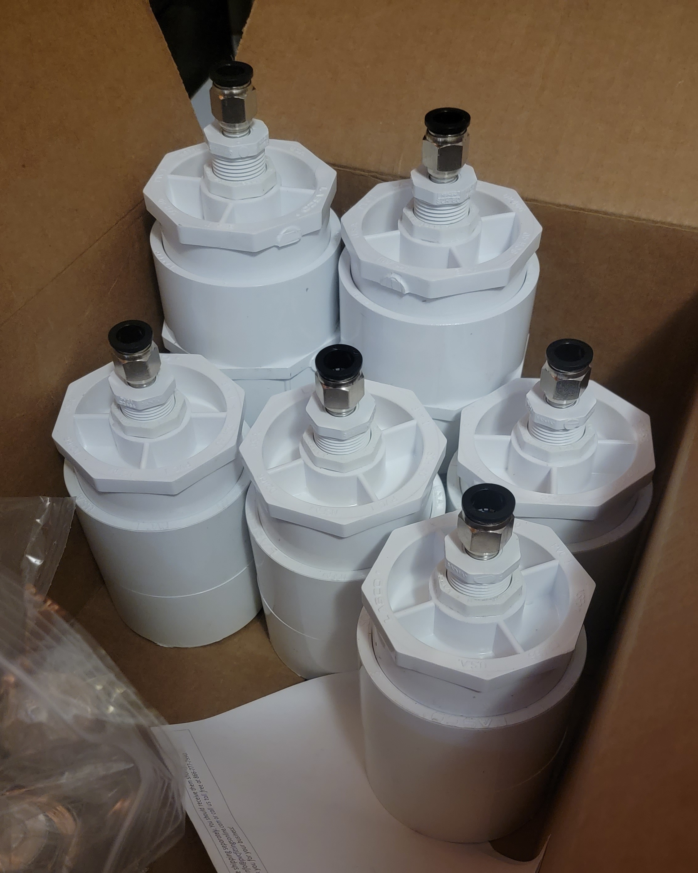 A box full of PVC assemblies made from bushings and push-connect air fittings